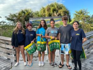 Five students smiling and holding bags of trash, promoting environmental awareness.