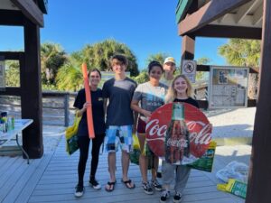 Four people on a wooden deck holding Coca Cola signs, showcasing their support for the brand.