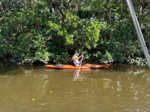 A woman kayaking on the water, propelling herself forward with a paddle.